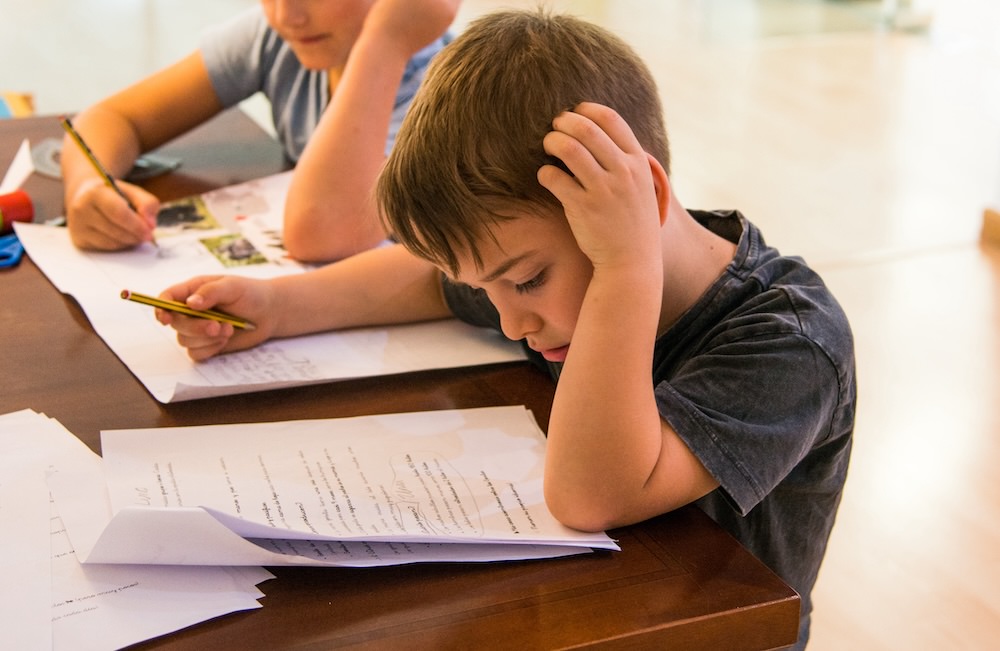 A very focused student doing writing tasks at a wooden table at the Second Body Montessori school in Valencia.